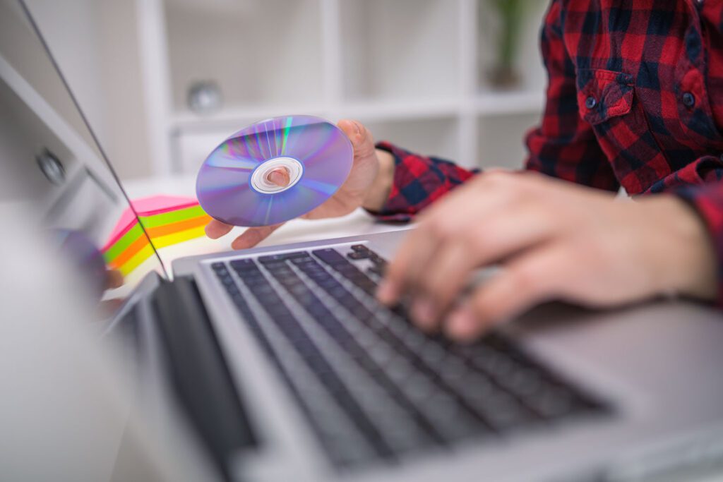 A person readying a DVD to watch on their laptop.